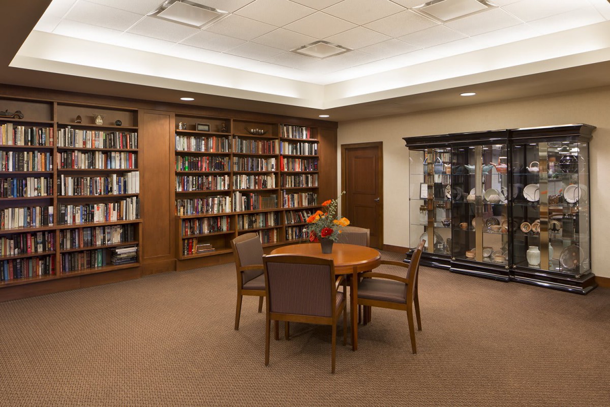 A cozy library with bookshelves, a central table, and chairs for reading.