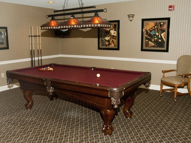 A stylish game room featuring a pool table with maroon felt, complete with cue sticks and overhead lighting.