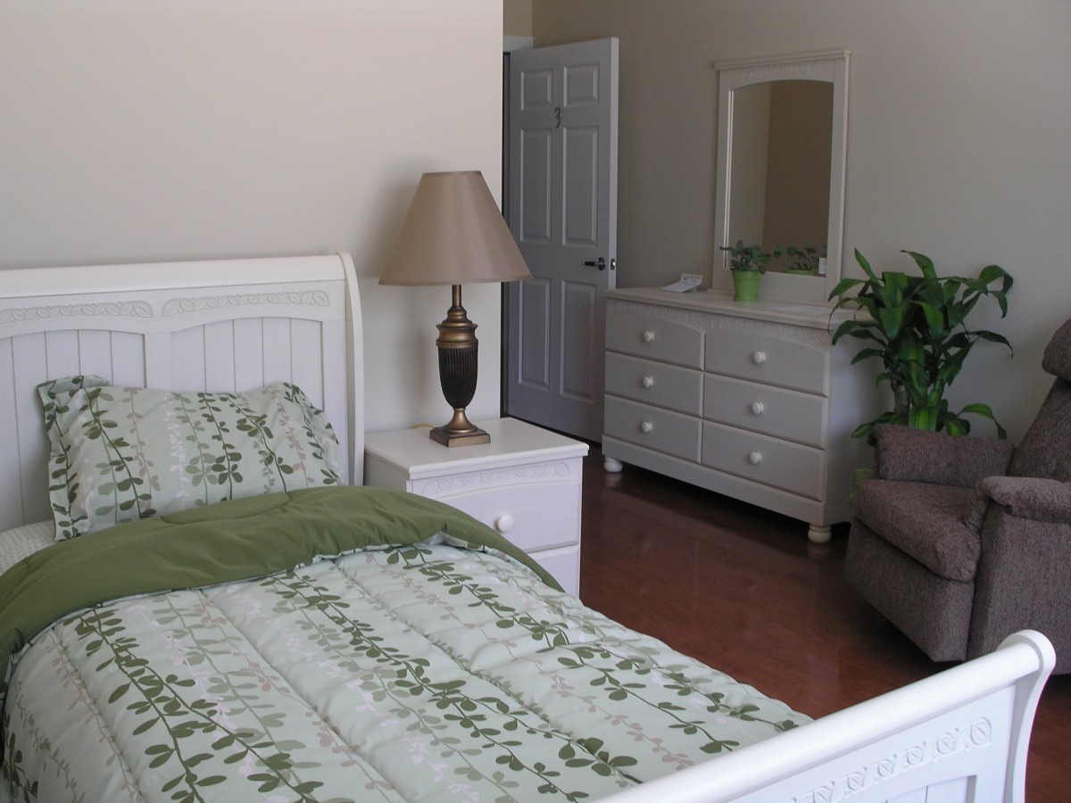 A cozy bedroom with a bed, dresser, lamp, and decorative green accents.