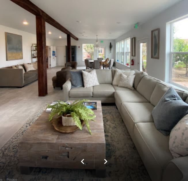 A spacious and well-lit living room featuring a large sectional sofa and a wooden coffee table, with an open floor plan leading to other areas of the home.