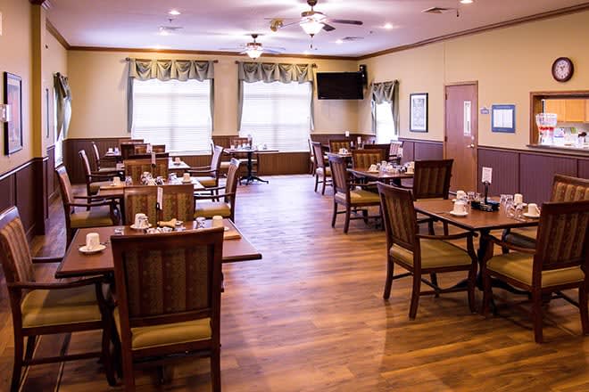 An empty restaurant dining room with wooden floors and neatly arranged tables and chairs.