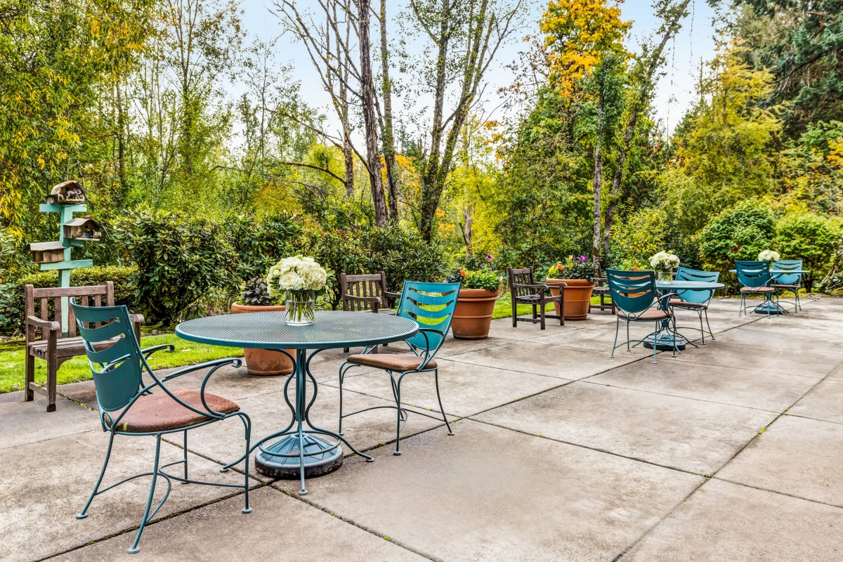 A tranquil outdoor patio with tables and chairs surrounded by lush greenery.