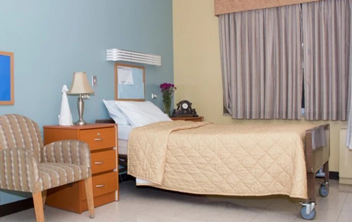 A hospital room with a bed, side table, lamp, and chair.