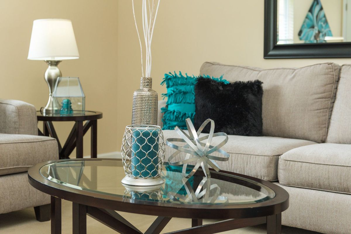 A modern living room with a glass coffee table, decorative pillows on the sofa, and stylish accents.