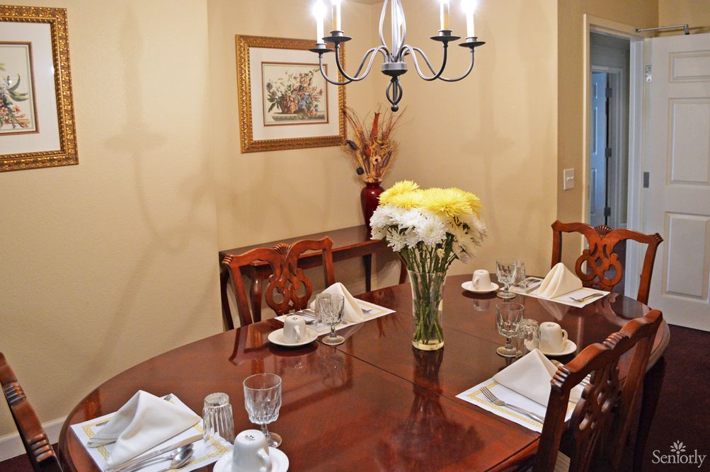 A neatly set dining table with flowers and a chandelier overhead.