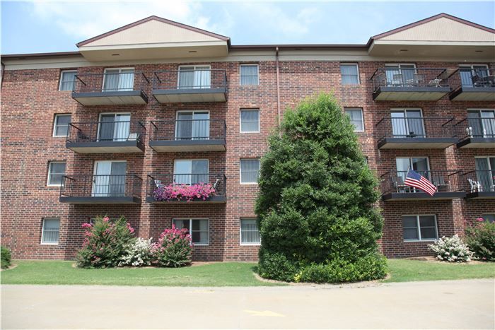 A brick apartment building with balconies and landscaped surroundings.