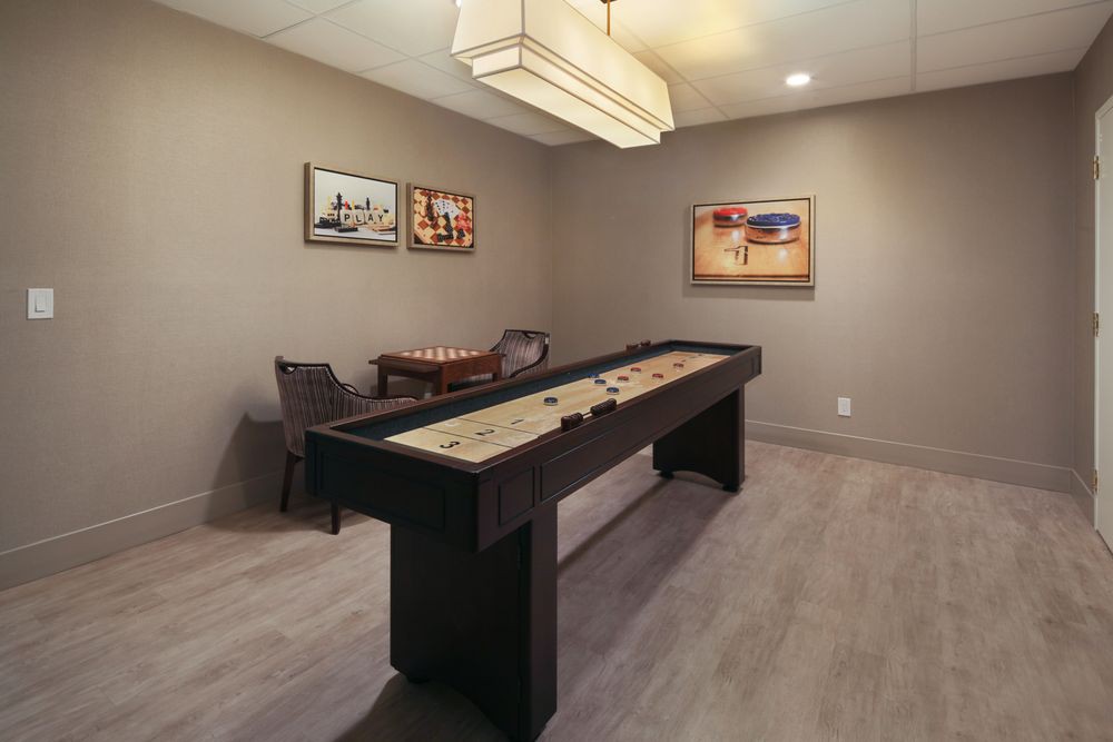 A modern game room featuring a shuffleboard table, comfortable seating, and stylish artwork.