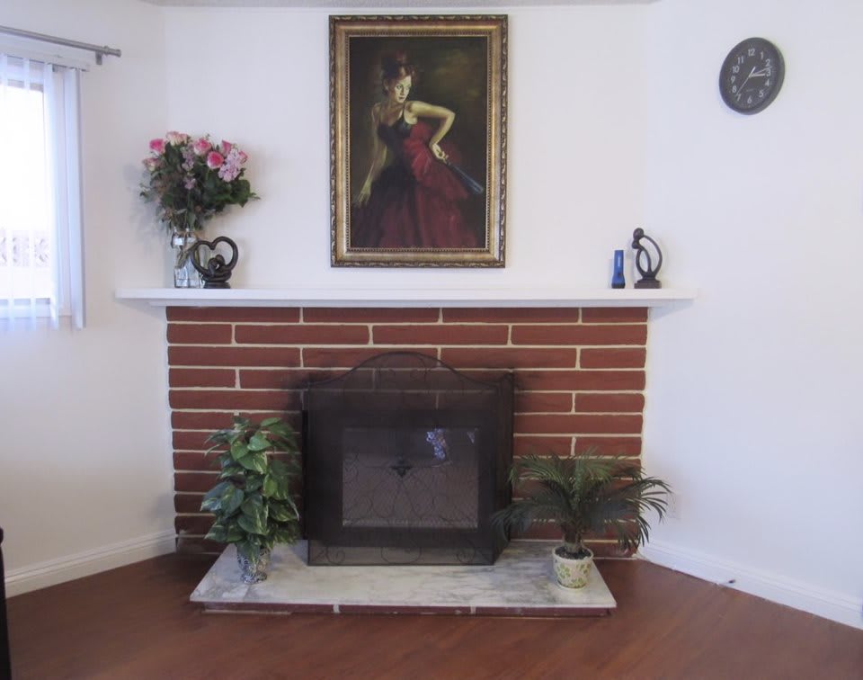 A cozy living room features a brick fireplace adorned with plants, flowers, and artwork.