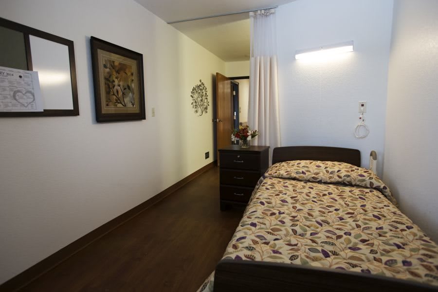 A cozy bedroom with a single bed, decorative paintings on the wall, and wooden flooring.
