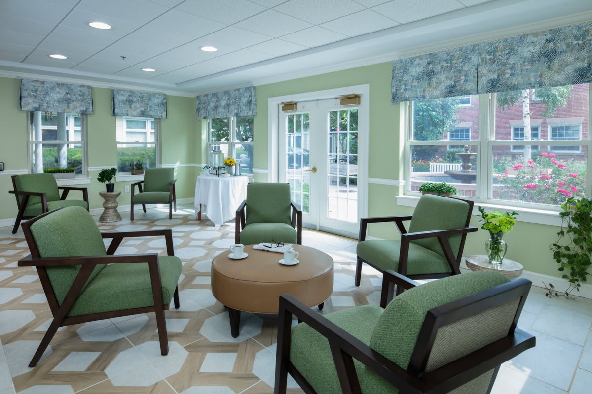 A cozy waiting area with green upholstered chairs and a round coffee table, well-lit by natural light from large windows.