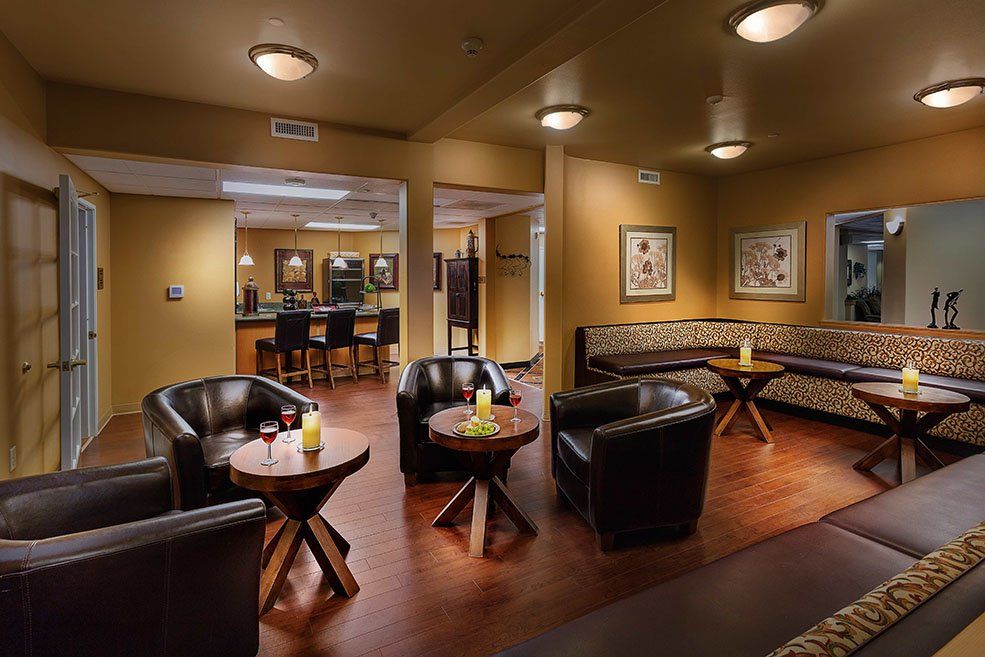 A cozy lounge area with leather chairs and tables, softly lit with wall artwork and wooden flooring.