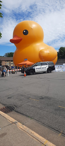 A giant inflatable rubber duck looms over a police vehicle at an outdoor event.