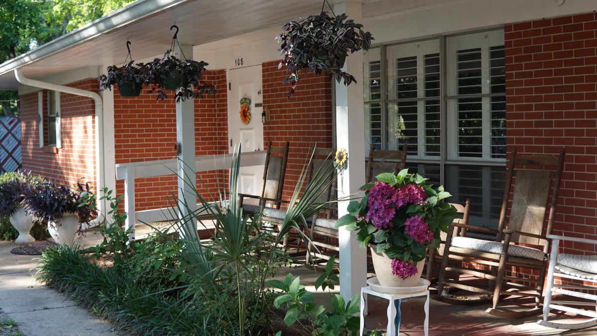 A cozy porch with rocking chairs and vibrant potted plants under a shaded roof.