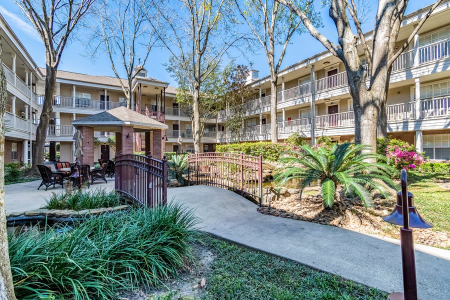 An exterior view of a multi-story apartment building with well-maintained landscaping and a central pathway.