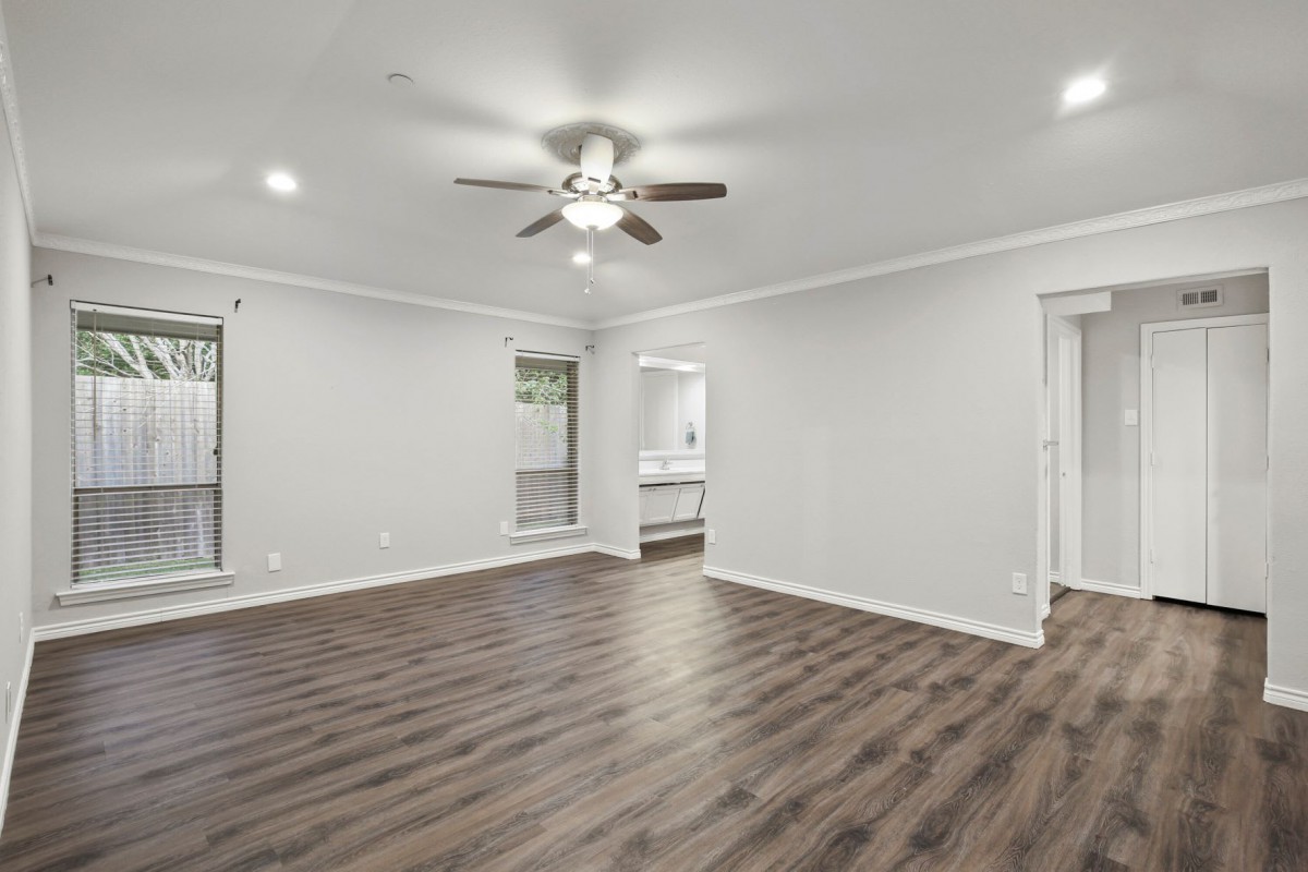 A spacious, empty living room with hardwood floors and a ceiling fan.