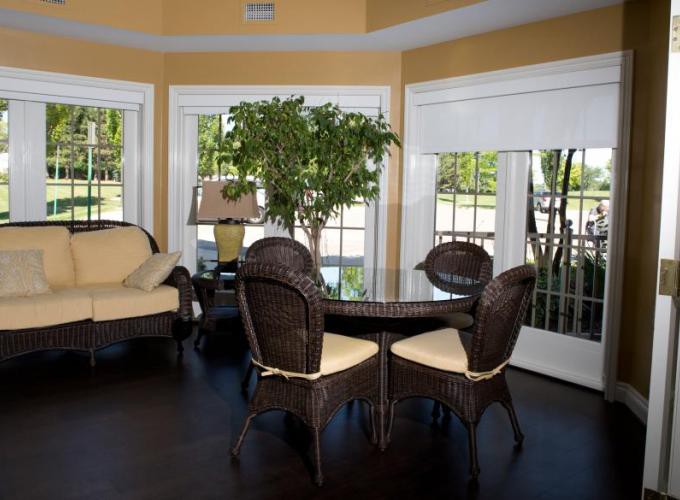 A cozy living room with wicker furniture, a glass table, and an indoor plant, bathed in natural sunlight.