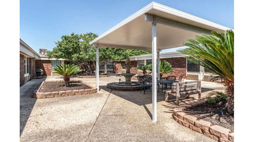 A cozy outdoor patio area featuring comfortable seating and a sunshade, surrounded by lush greenery.