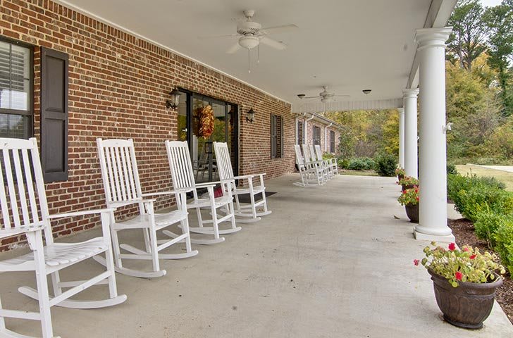 A peaceful porch with white rocking chairs and ceiling fans, perfect for relaxation.