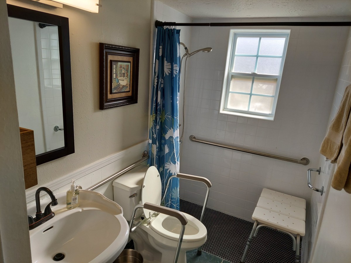An accessible bathroom with grab bars, a shower bench, and a blue shower curtain.