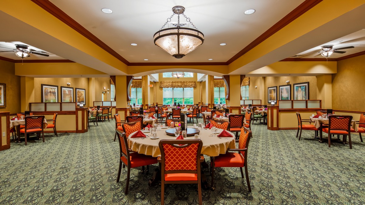 An elegant dining room with neatly arranged tables and chairs, featuring a large chandelier overhead.