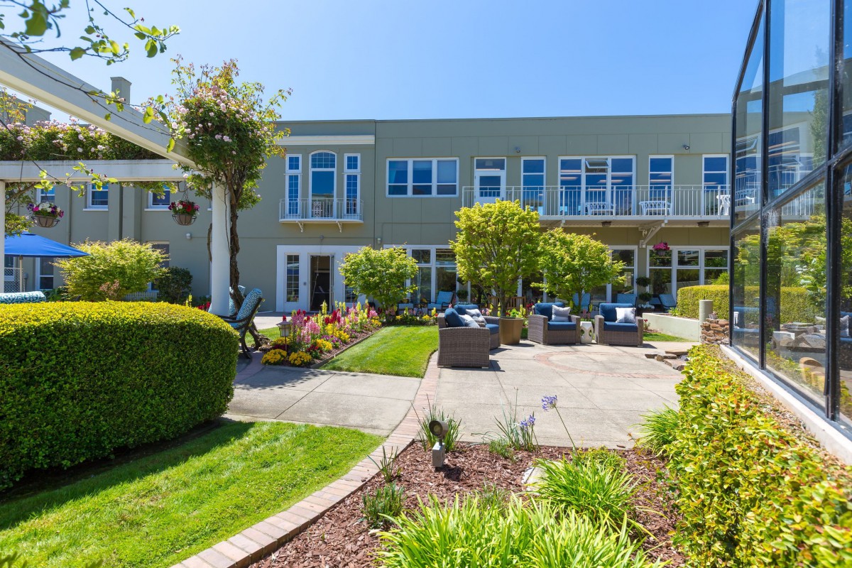 A sunny view of a landscaped garden with outdoor seating in front of a modern residential building.