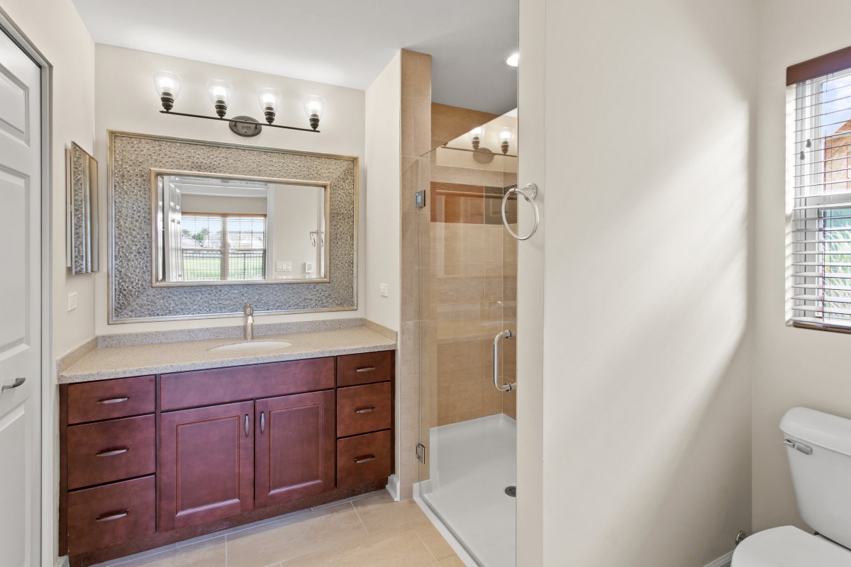 A modern bathroom featuring a wooden vanity with a large mirror and overhead lighting, alongside a spacious shower area.