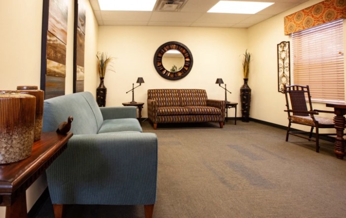 A well-lit waiting room with sofas, a wall mirror, and decorative elements.