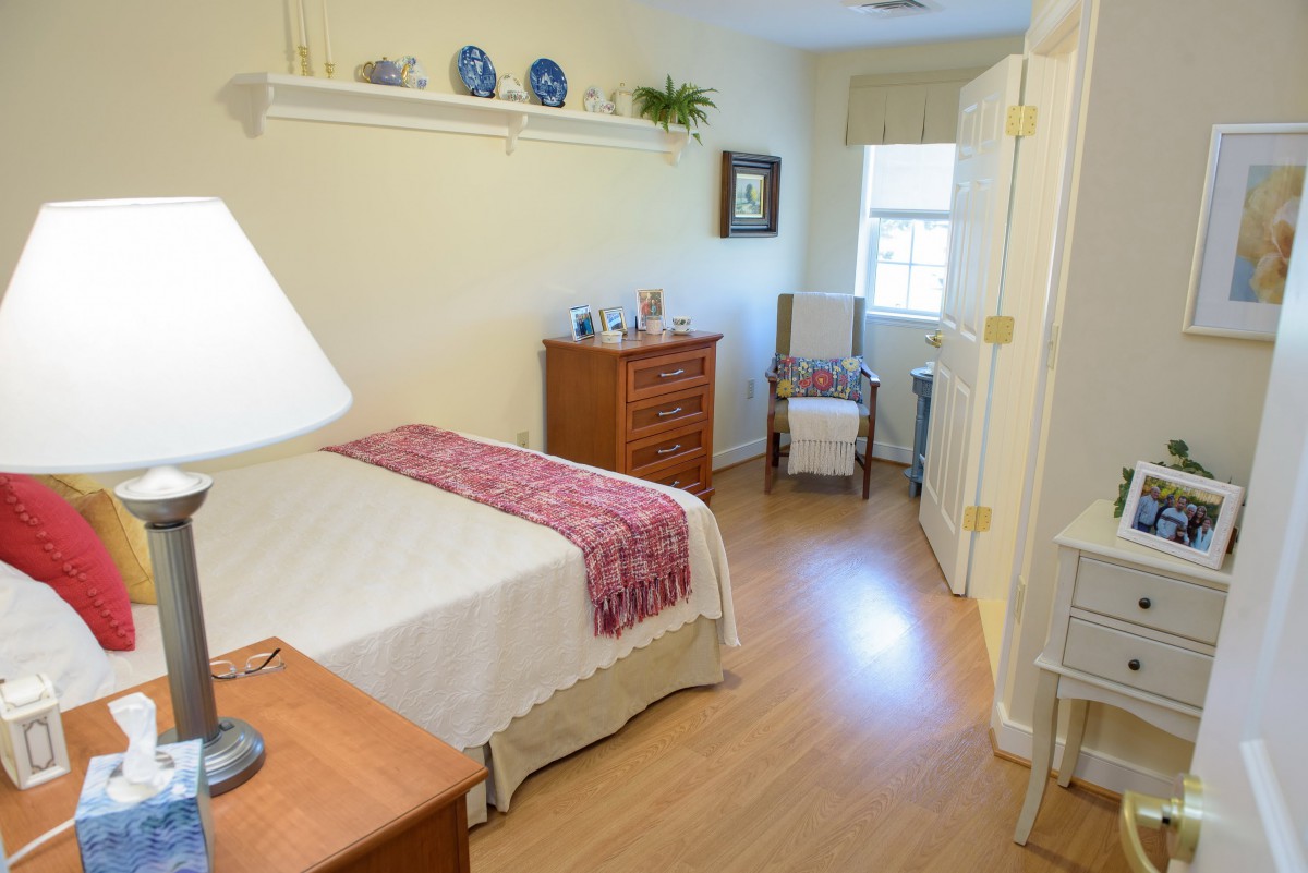 A cozy bedroom with light-colored walls, a bed, and a window letting in natural light.