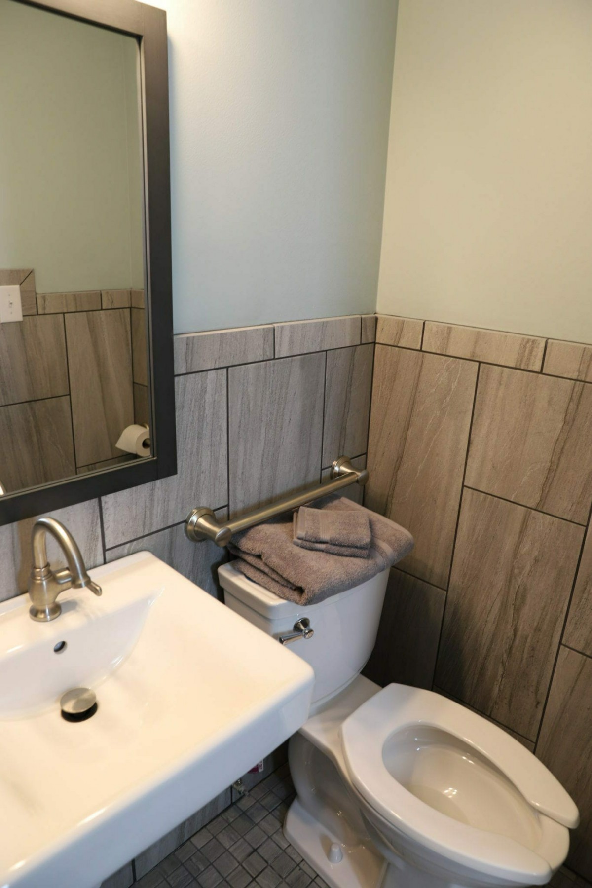 A modern bathroom with a sink, mirror, and neatly folded towels on the toilet.