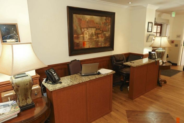 A reception area with wooden desks, laptops, and a telephone, adorned with artwork on the wall.