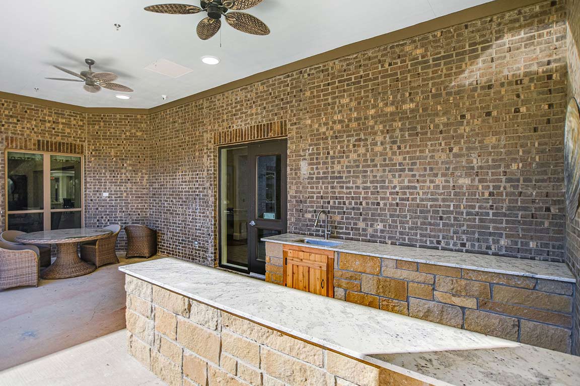 An outdoor kitchen with a stone bar counter, brick walls, and ceiling fans.