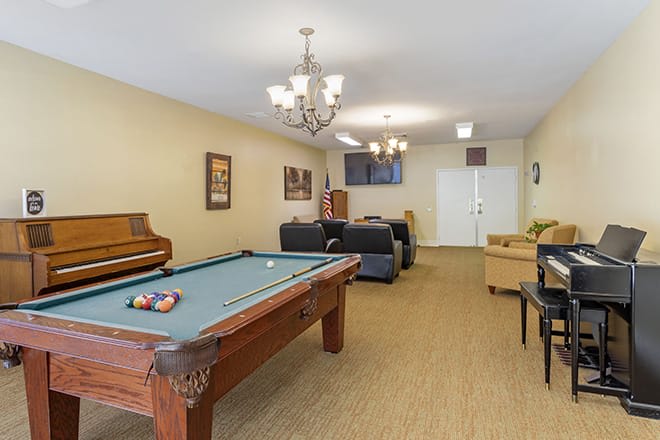 A cozy game room featuring a pool table, sofas, a piano, and a television.