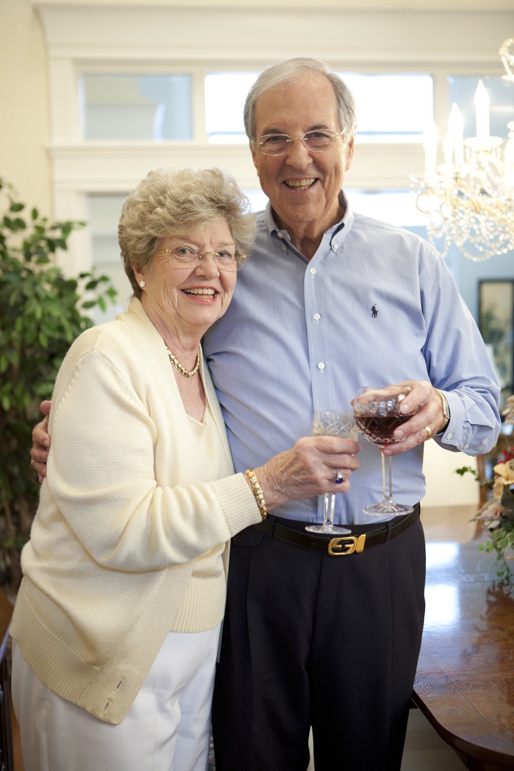 An elderly couple smiling and holding wine glasses indoors.