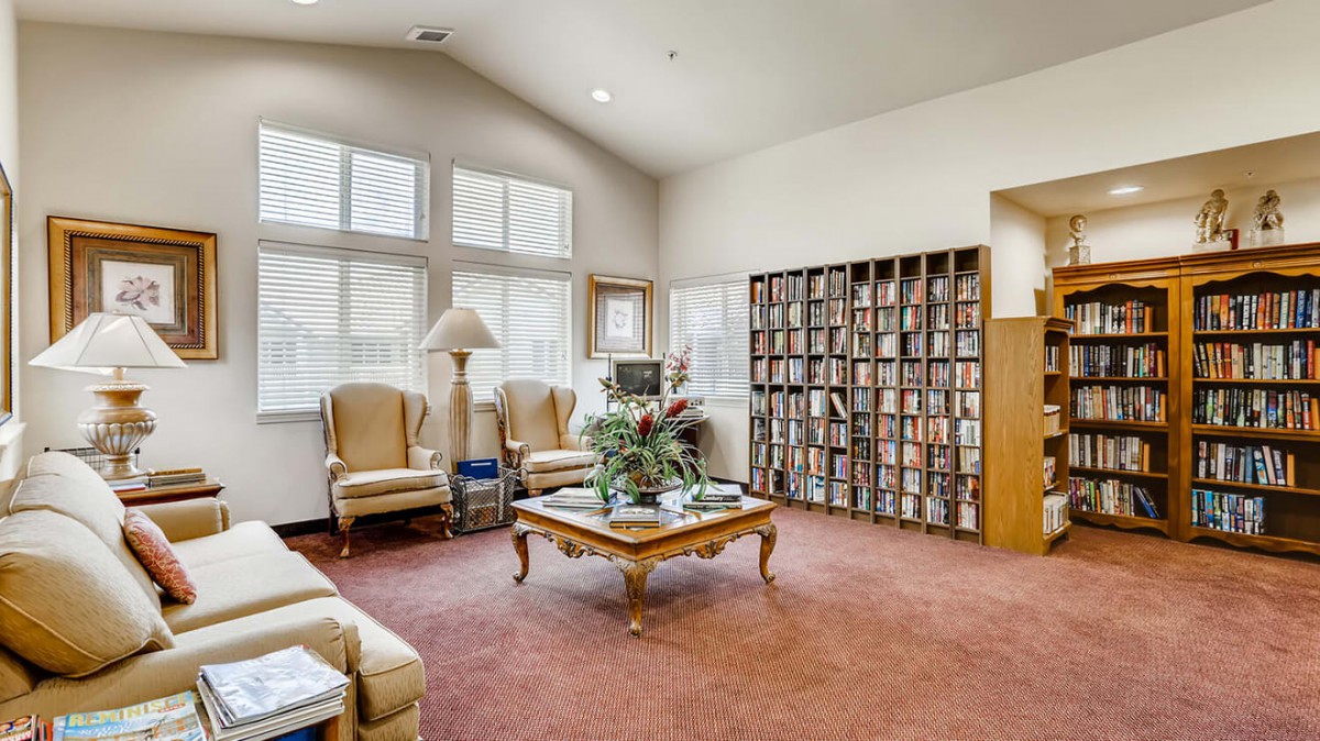 A cozy library room with a large bookshelf, comfortable chairs, and natural light coming through the windows.