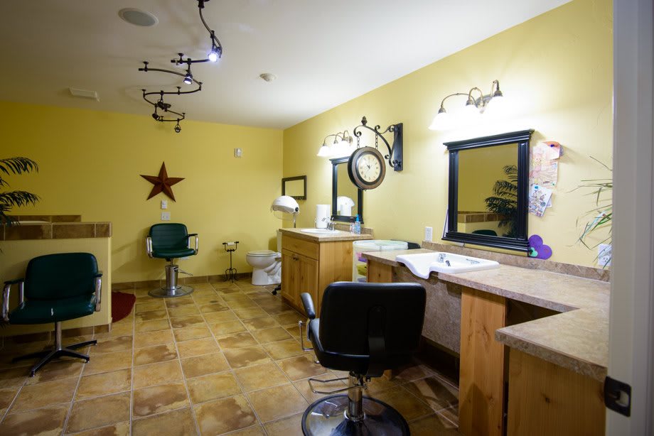 A well-lit beauty salon interior with yellow walls, featuring multiple styling stations and chairs.