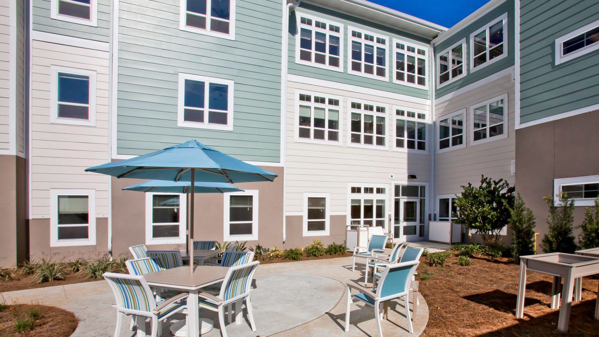 A residential building with an outdoor patio area featuring tables, chairs, and a large umbrella.