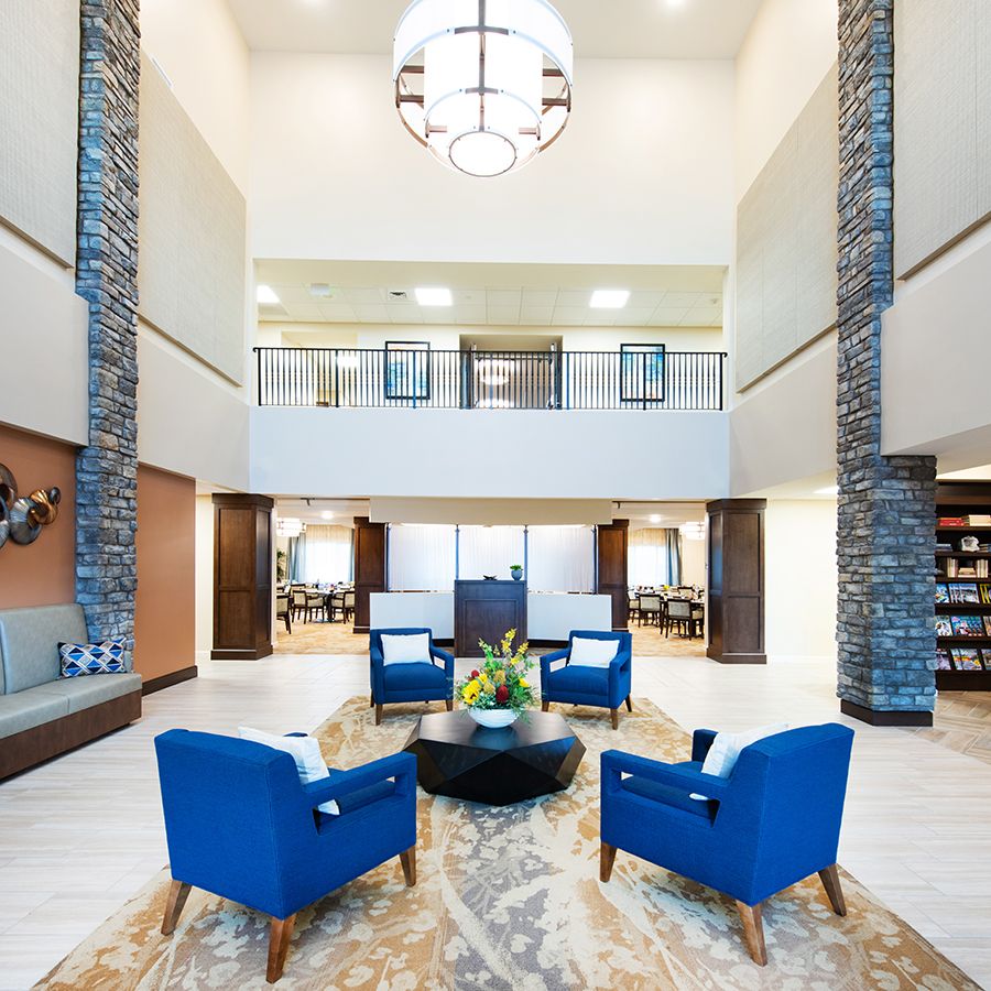 A modern lobby featuring blue chairs, tall ceilings, and elegant lighting.