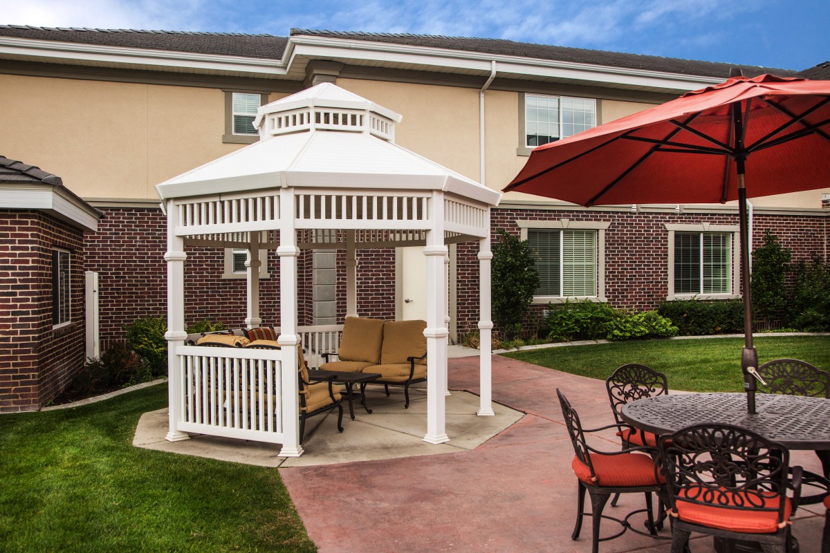 A cozy outdoor patio featuring a white gazebo with seating and a large red umbrella nearby.