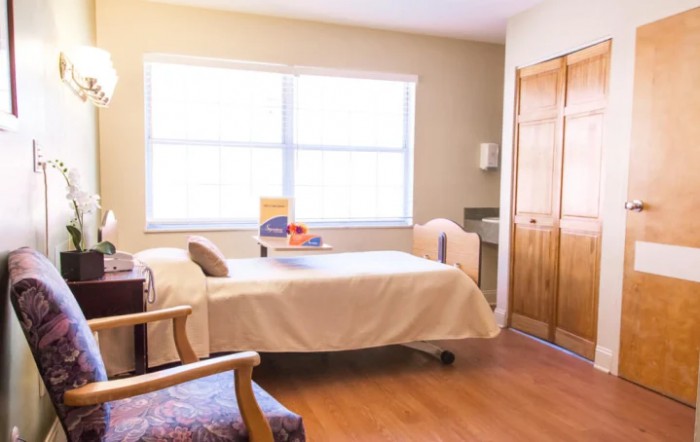 A bright and simple bedroom with a bed, chair, and wardrobe.