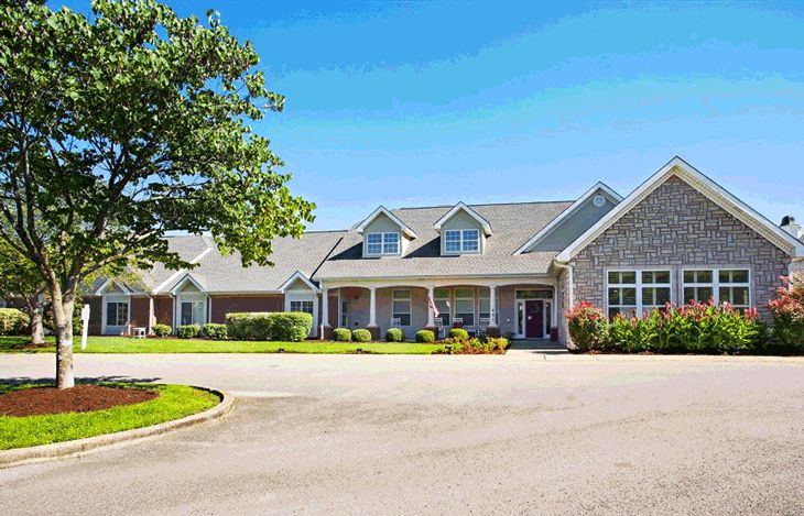 A large residential-style building with a neatly paved driveway and surrounding greenery against a clear blue sky.