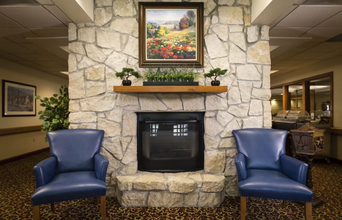 A cozy living room with a stone fireplace, adorned by a colorful painting and flanked by two blue chairs.