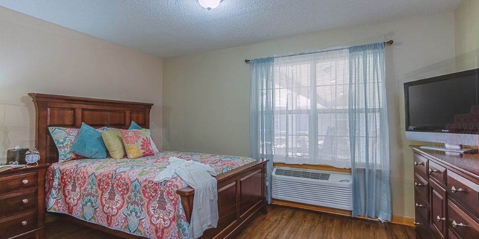 A cozy bedroom with a large window and colorful bedding.