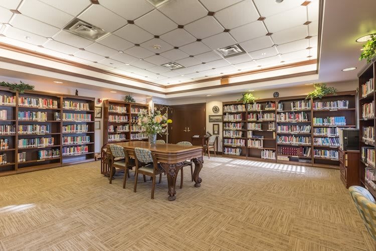 A cozy library reading area with shelves full of books and a central table with chairs.