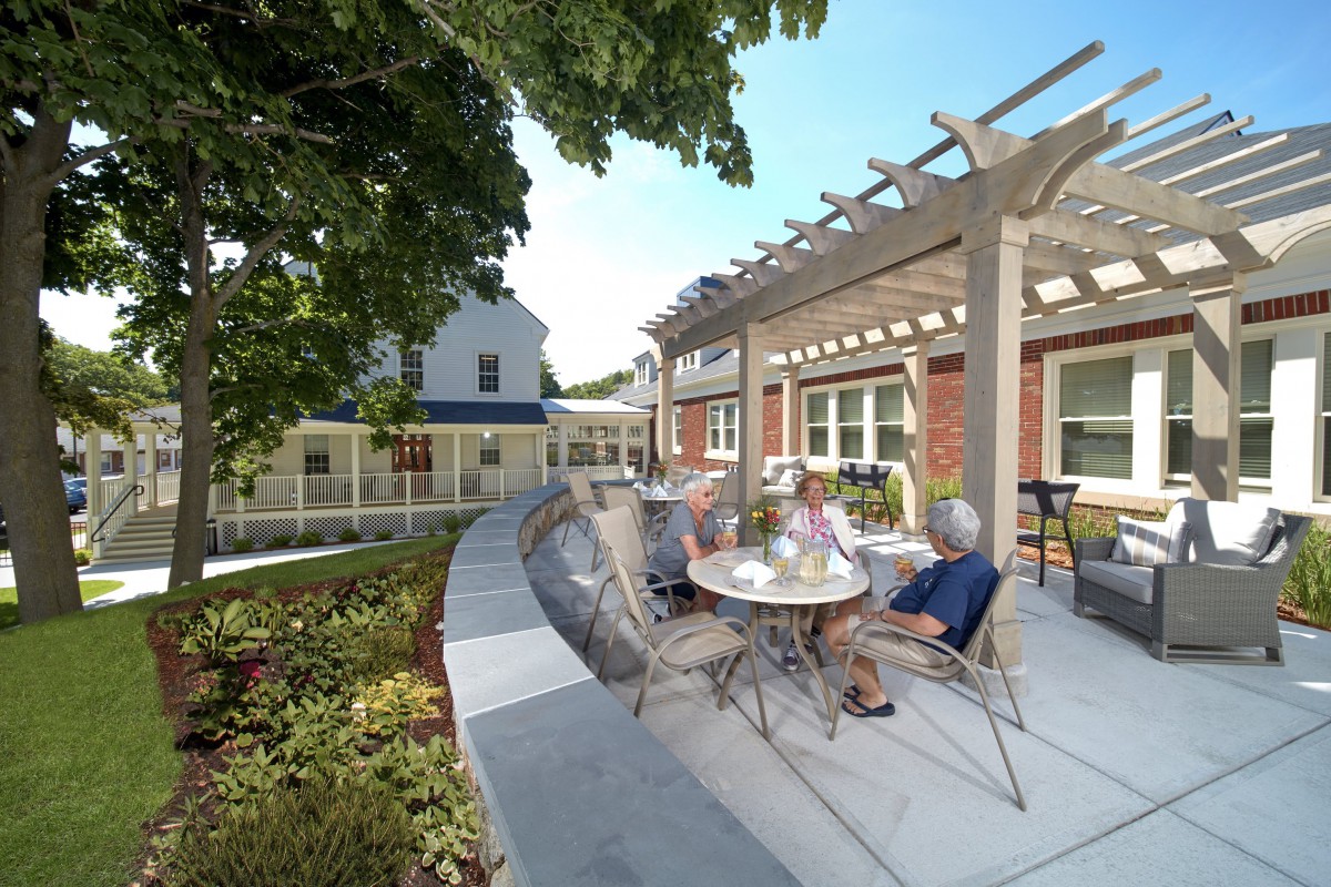 A group of elderly people enjoying a sunny day on an outdoor patio with a pergola.