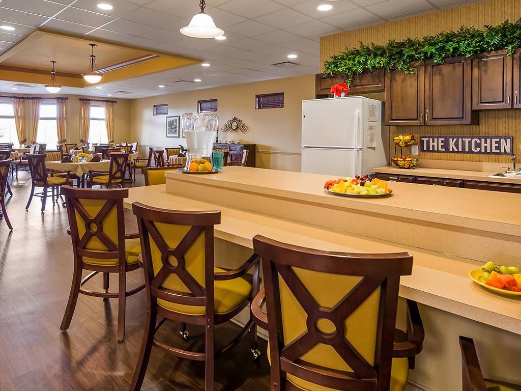 A cozy kitchen and dining area featuring a bar counter with elegant chairs, a refrigerator, and warm lighting.