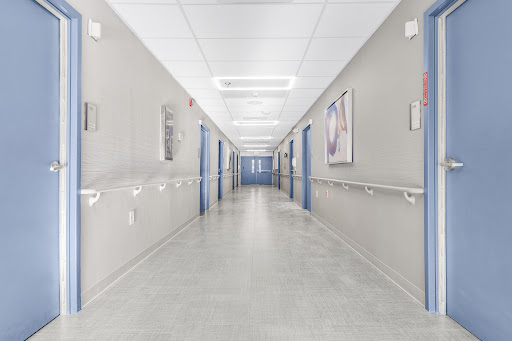 A spacious and well-lit corridor in a hospital, featuring blue doors and minimalist design.