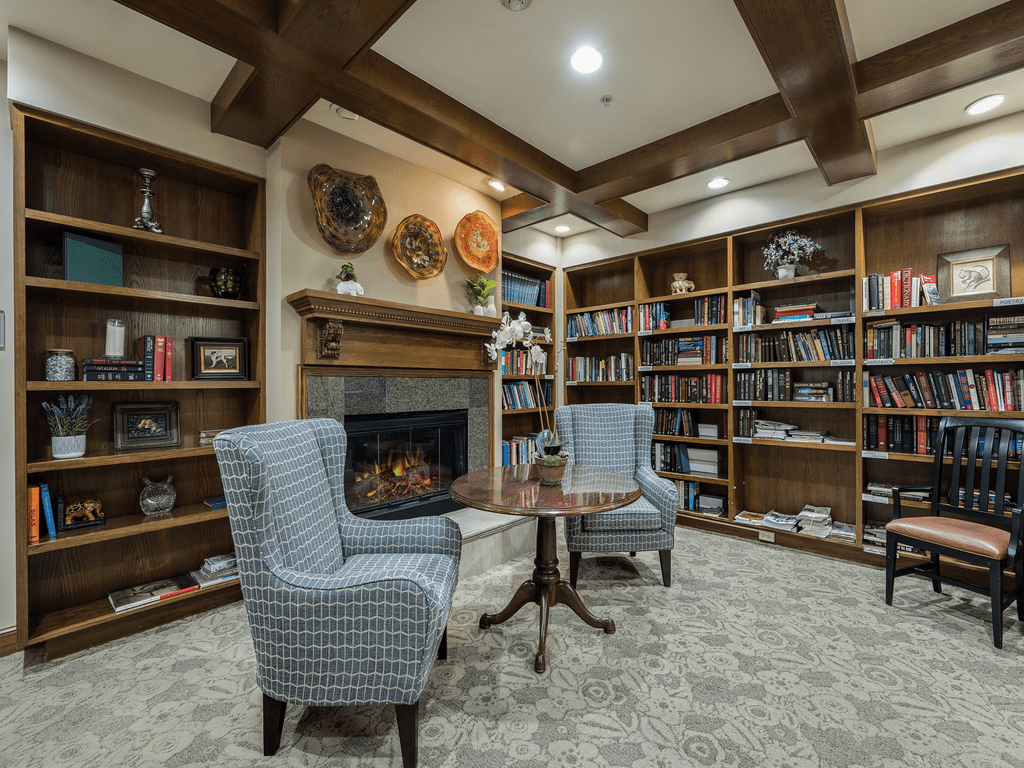 A cozy library room with bookshelves, a fireplace, and comfortable seating.