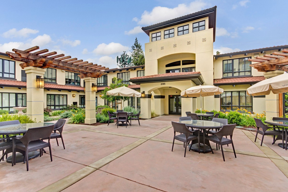 A courtyard with outdoor seating and umbrellas in front of a large building on a sunny day.