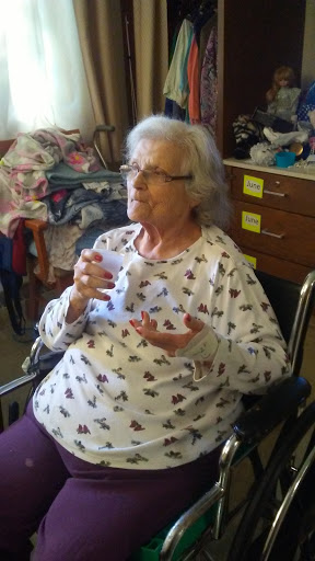 An elderly woman sitting in a wheelchair, enjoying a moment with a cup in her hand.