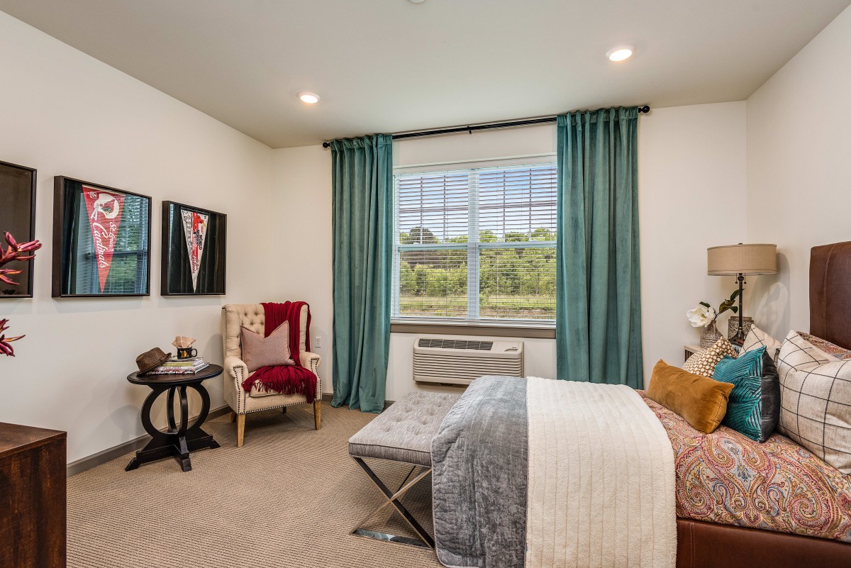 A modern bedroom with an armchair, window with teal curtains, and stylish decor.